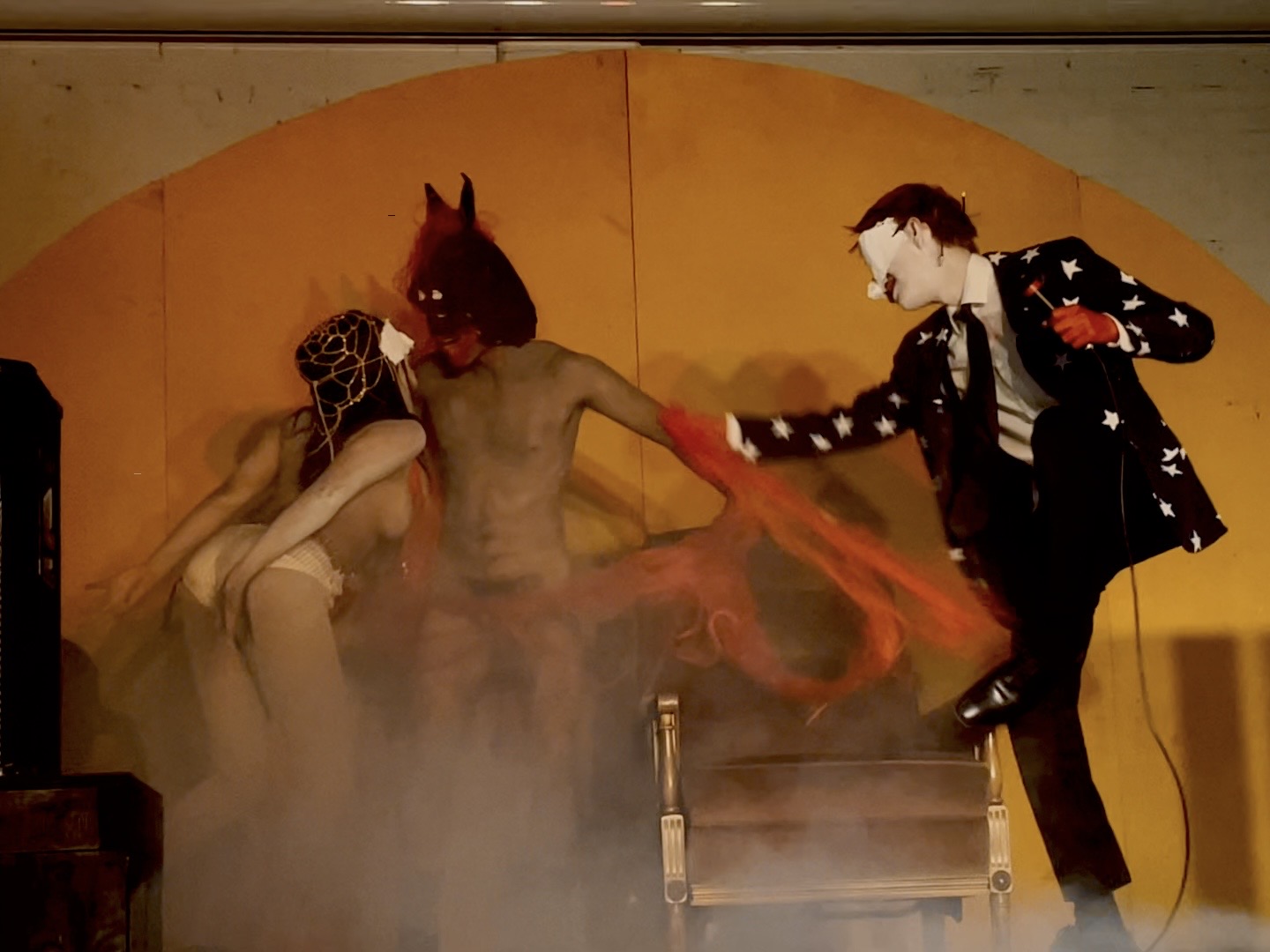 A naked woman and man dance around a throne, a clown dances beside them