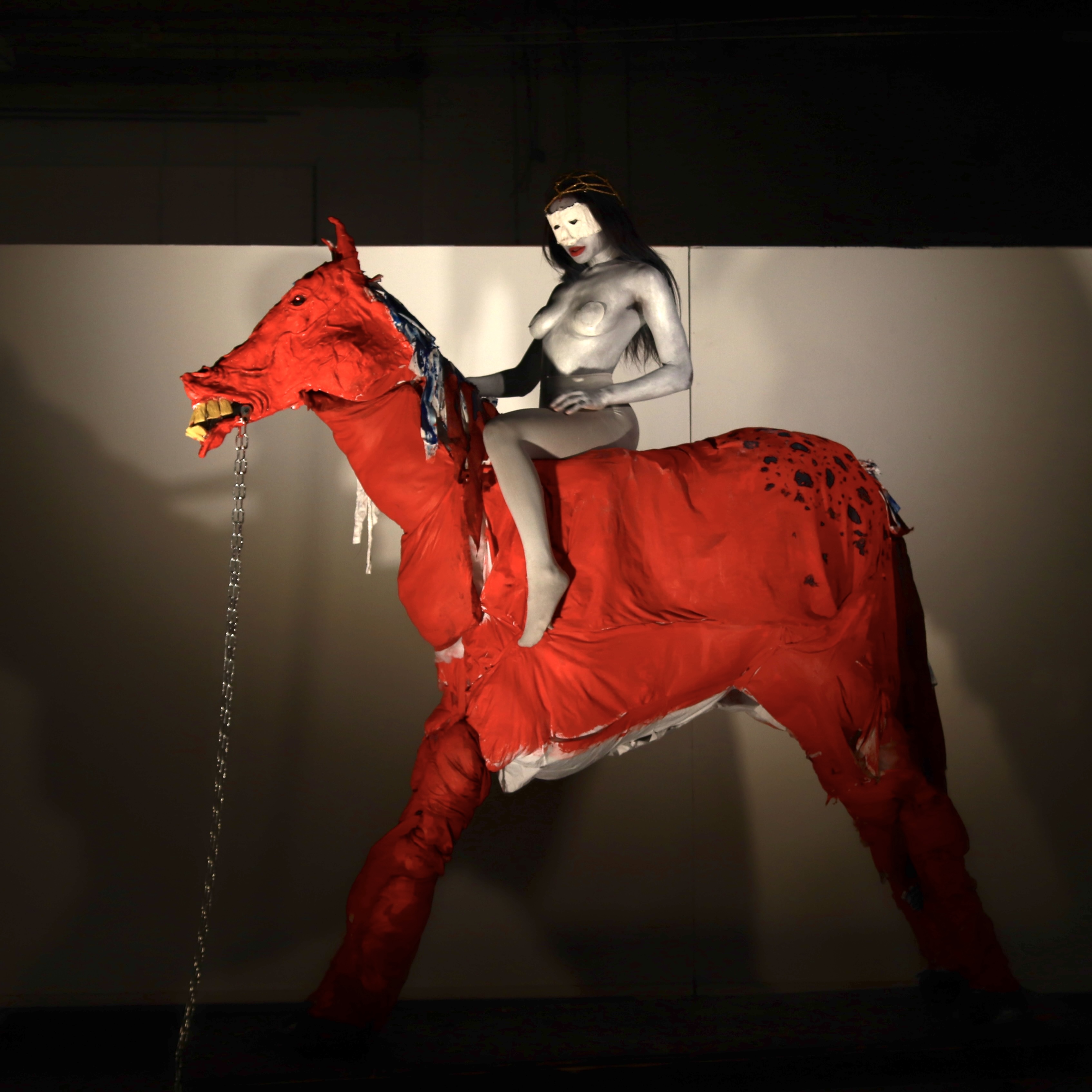 A topless woman painted white sits atop a bright red horse