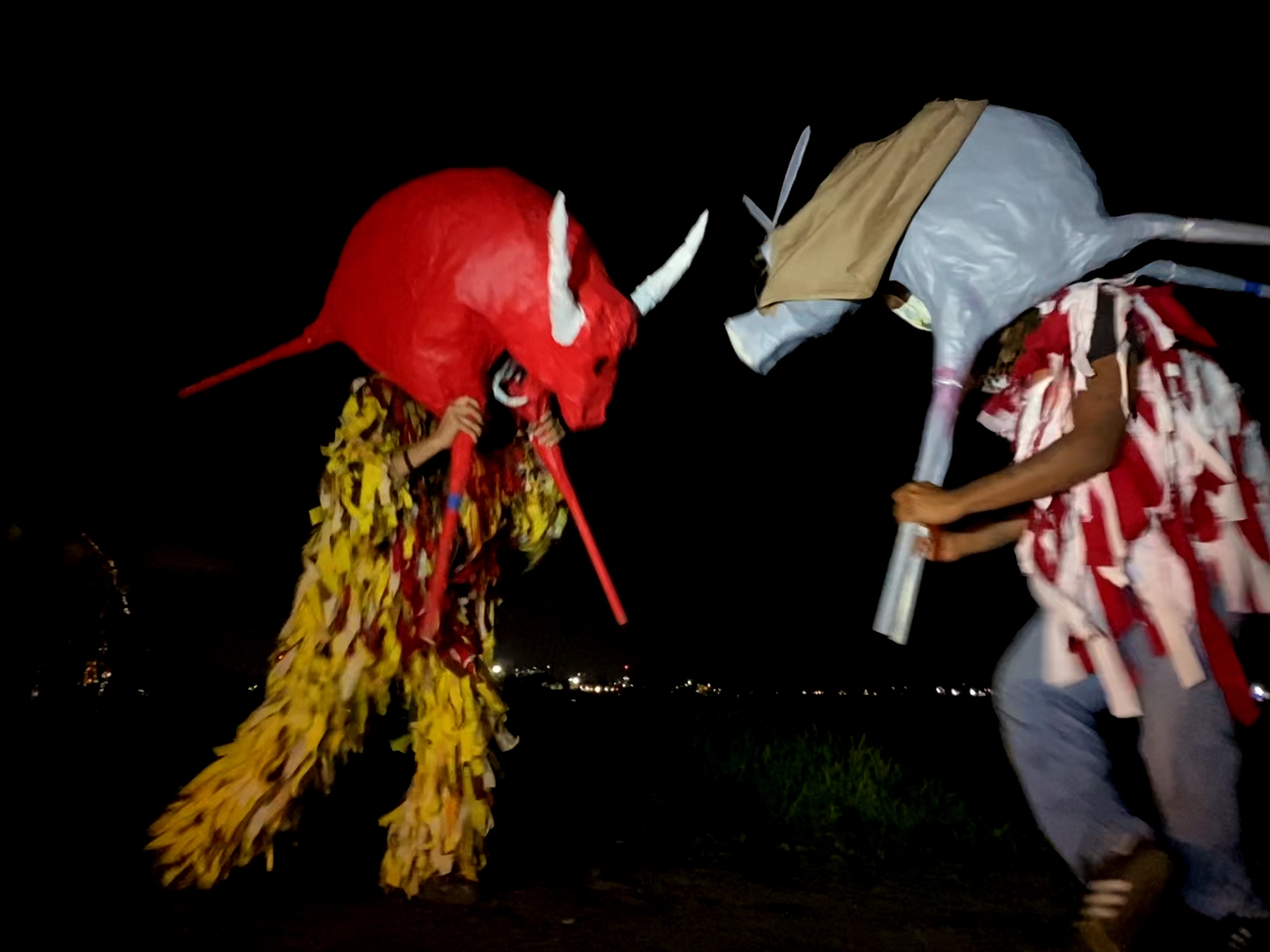 Two costumed figures carrying animal sculptures over their head fighting